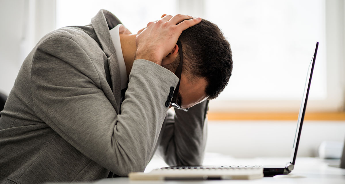 Man holding hands behind lowered head over a computer